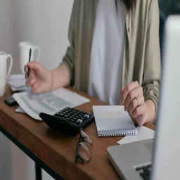 Someone does accounting with a laptop and paperwork.