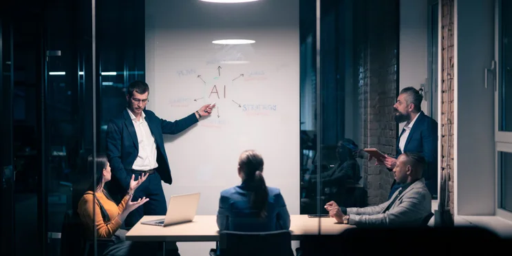 Workers sitting in office with AI written on whiteboard