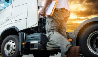 Driver with clipboard walking up to truck with sunset in background