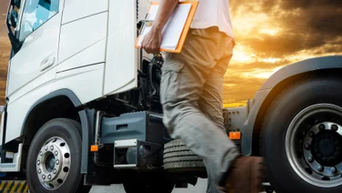 Driver with clipboard walking up to truck with sunset in background
