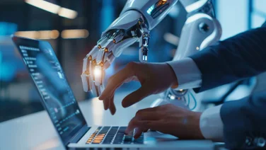 Person working on laptop, assisted by robot