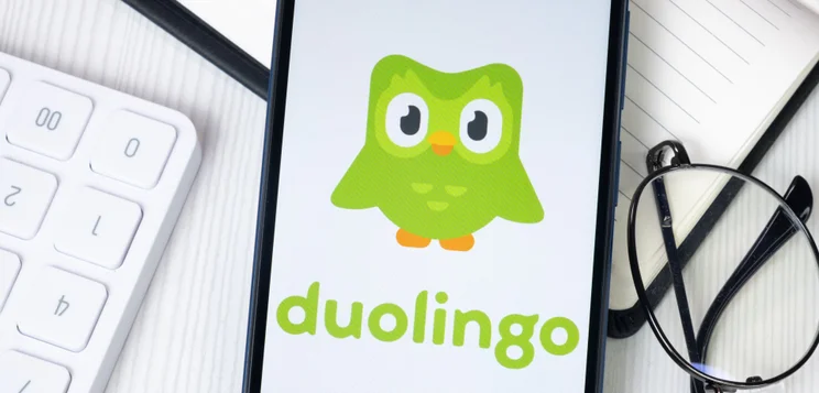 Duolingo logo on phone on desk with glasses and keyboard