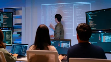 Workers in dark room with code on wall and on laptops