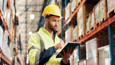 Man in factory wearing hard hat looking up details on tablet