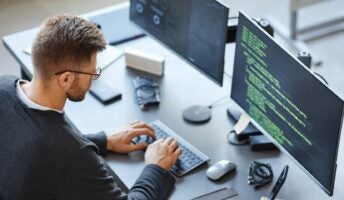 Engineer on desk with dual monitors working on code