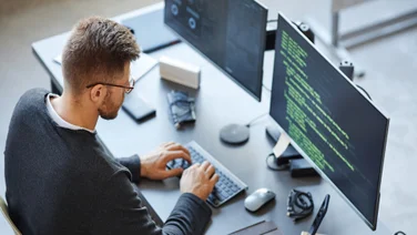 Engineer on desk with dual monitors working on code
