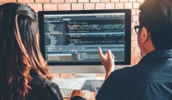 Man and woman looking at code on a laptop sat at desk