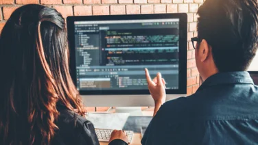 Man and woman looking at code on a laptop sat at a desk. Source: Tech.co Testing