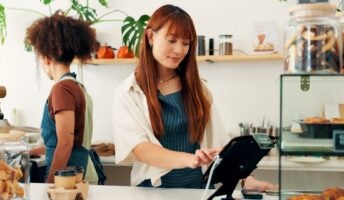 Worker using POS system in small cafe with employee behind