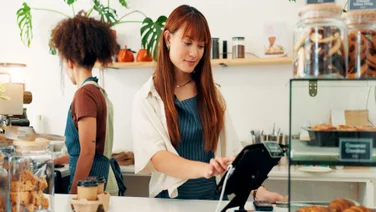 Worker using POS system in small cafe with employee behind