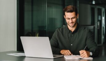 Smiling young man working at desk in office with laptop