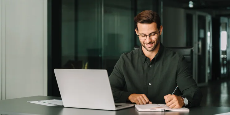 Smiling young man working at desk in office with laptop