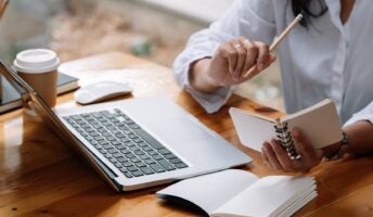 Individual working with laptop on desk with notebooks
