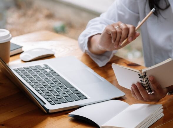 Individual working with laptop on desk with notebooks