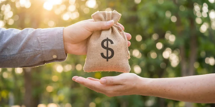 Person handing other person bag with dollar sign